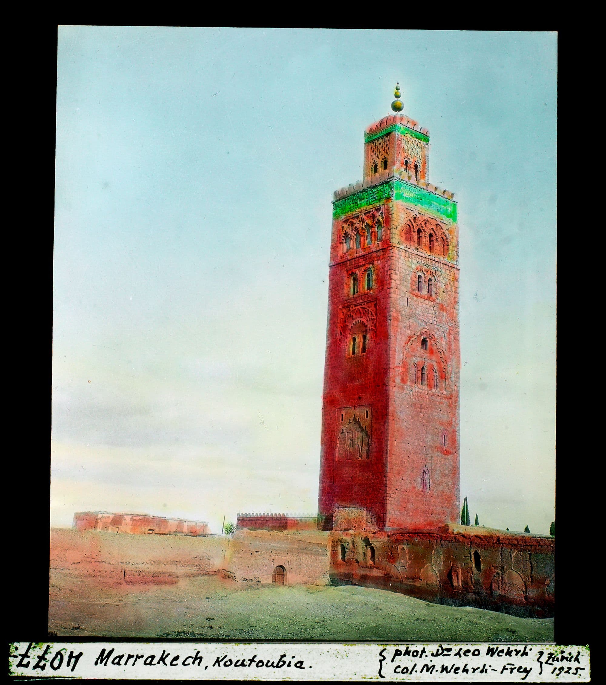 Le minaret de la Koutoubia, tour carrée aux façades rouges surmontée d'un lanternon vert, au-dessus d'un mur bas.