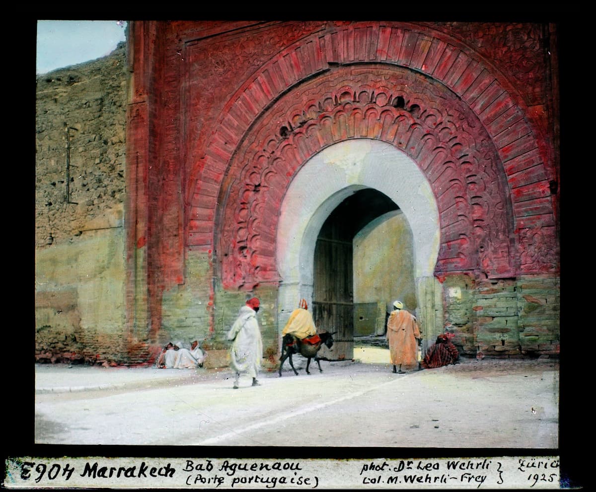 Le grand arc de Bab Agnaou au décor sculpté rouge, avec des passants et un âne devant l'entrée.