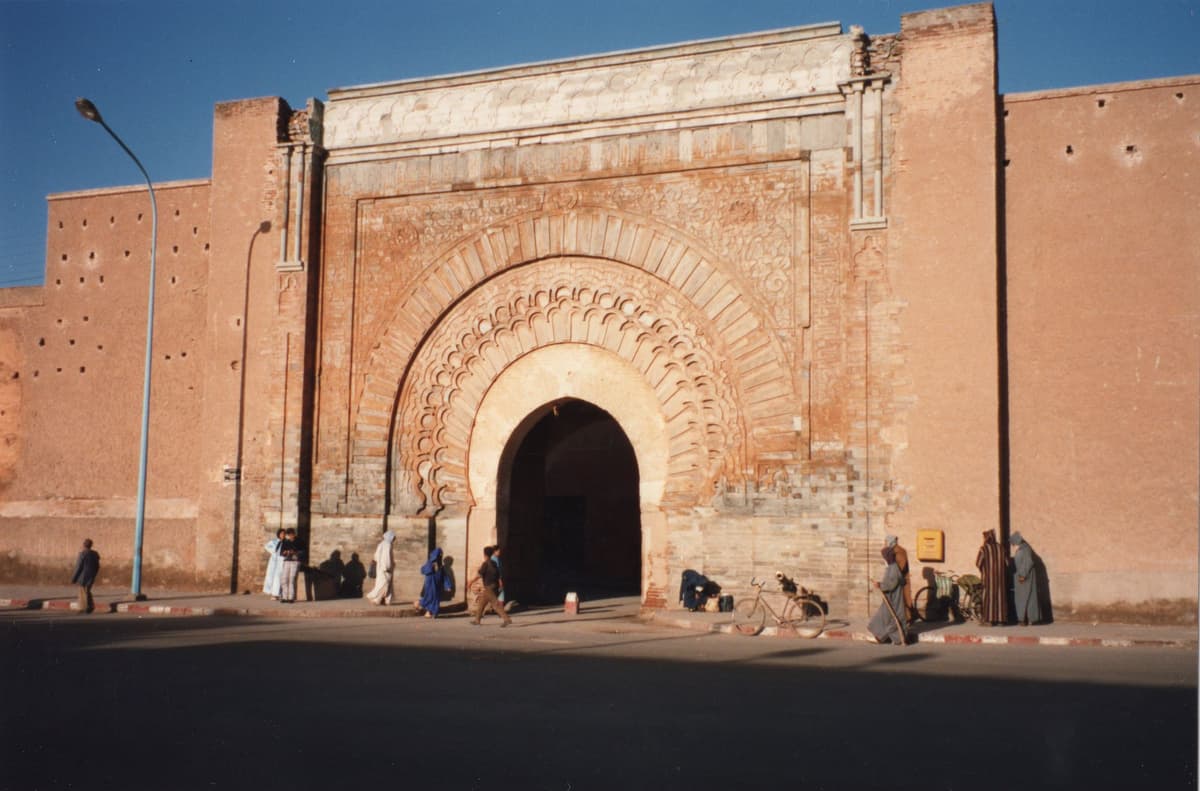 L'arc sculpté de Bab Agnaou dans le rempart ocre, avec des passants et des vélos au pied du mur.