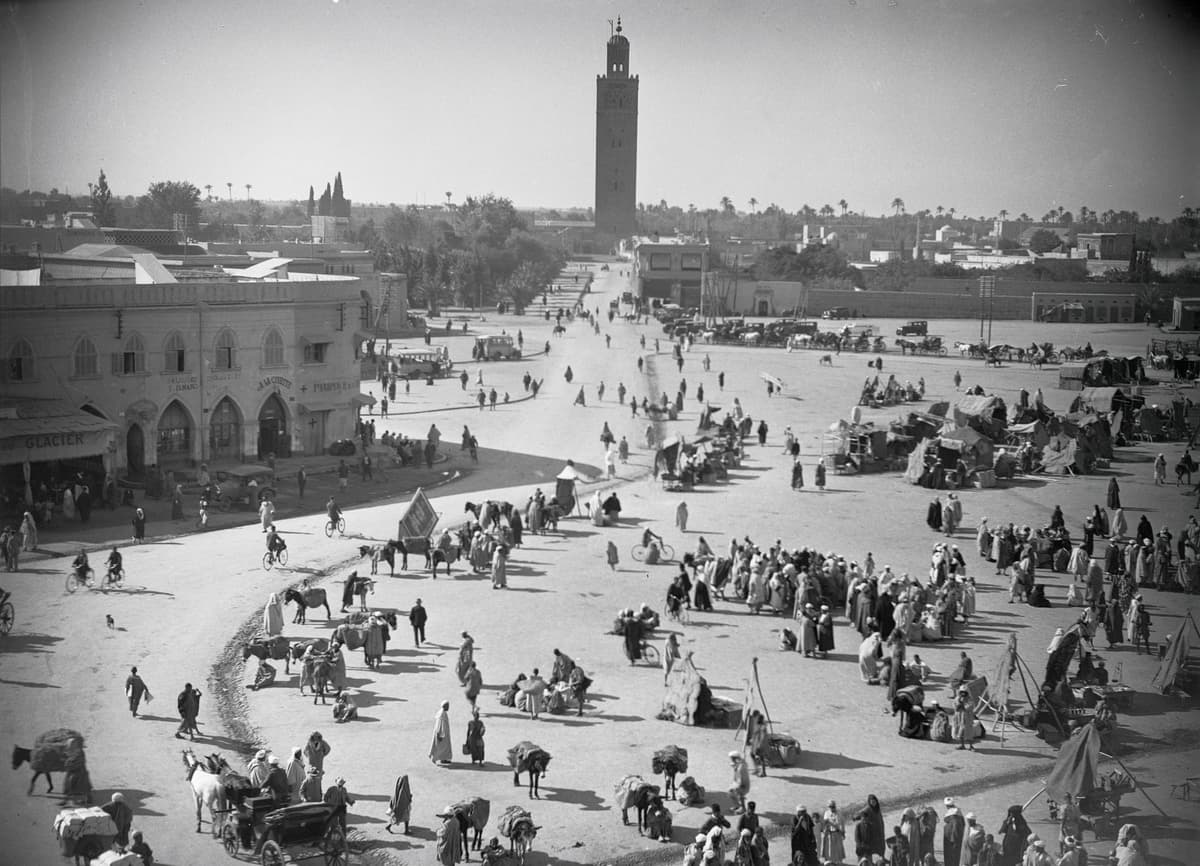 La place vue d'en haut : foule, tentes et calèches, avec le minaret de la Koutoubia au fond.