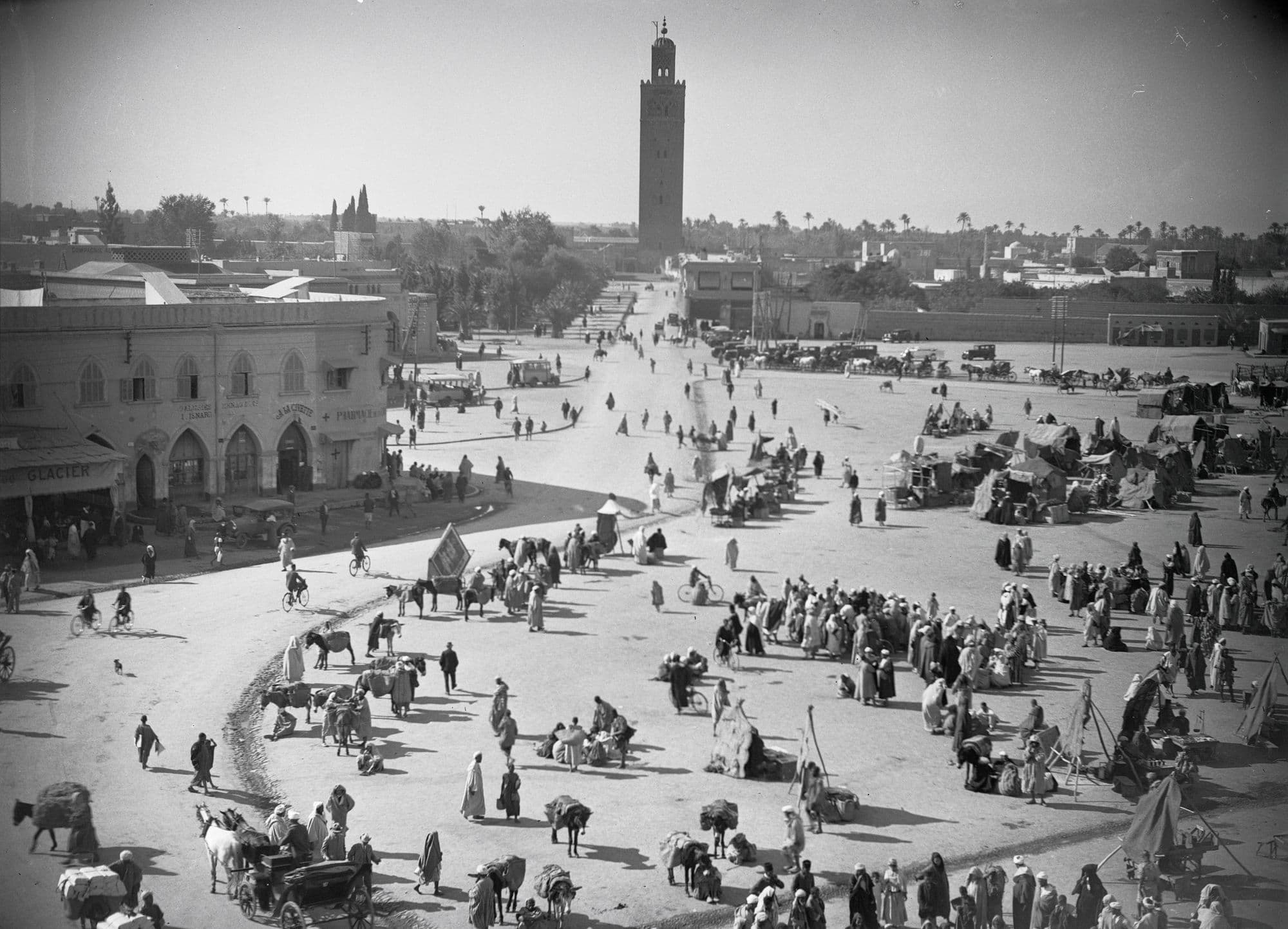 La place vue d'en haut : foule, tentes et calèches, avec le minaret de la Koutoubia au fond.