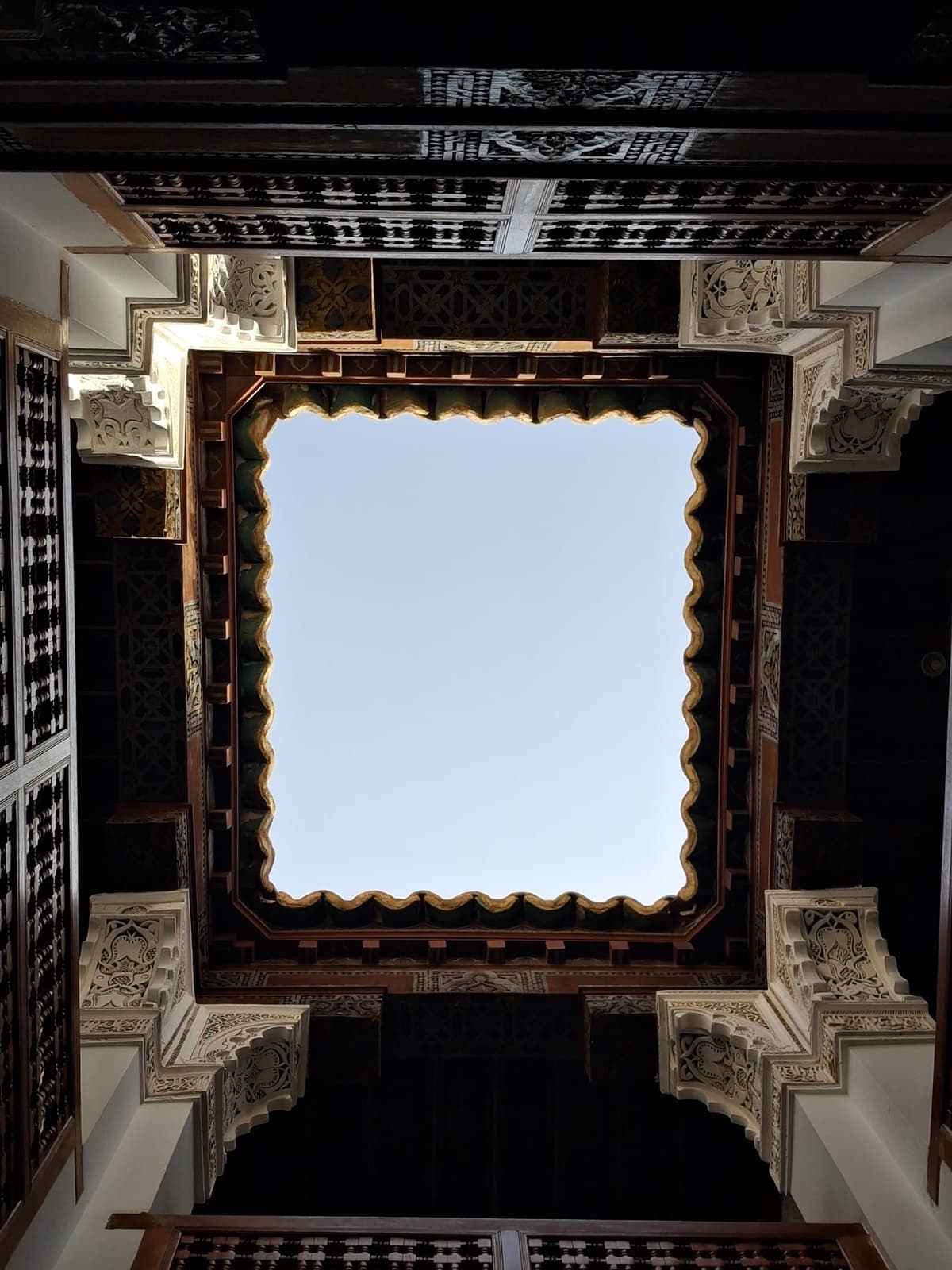 Plafond de cèdre sculpté ouvert sur le ciel, vu depuis la cour de la médersa Ben Youssef.