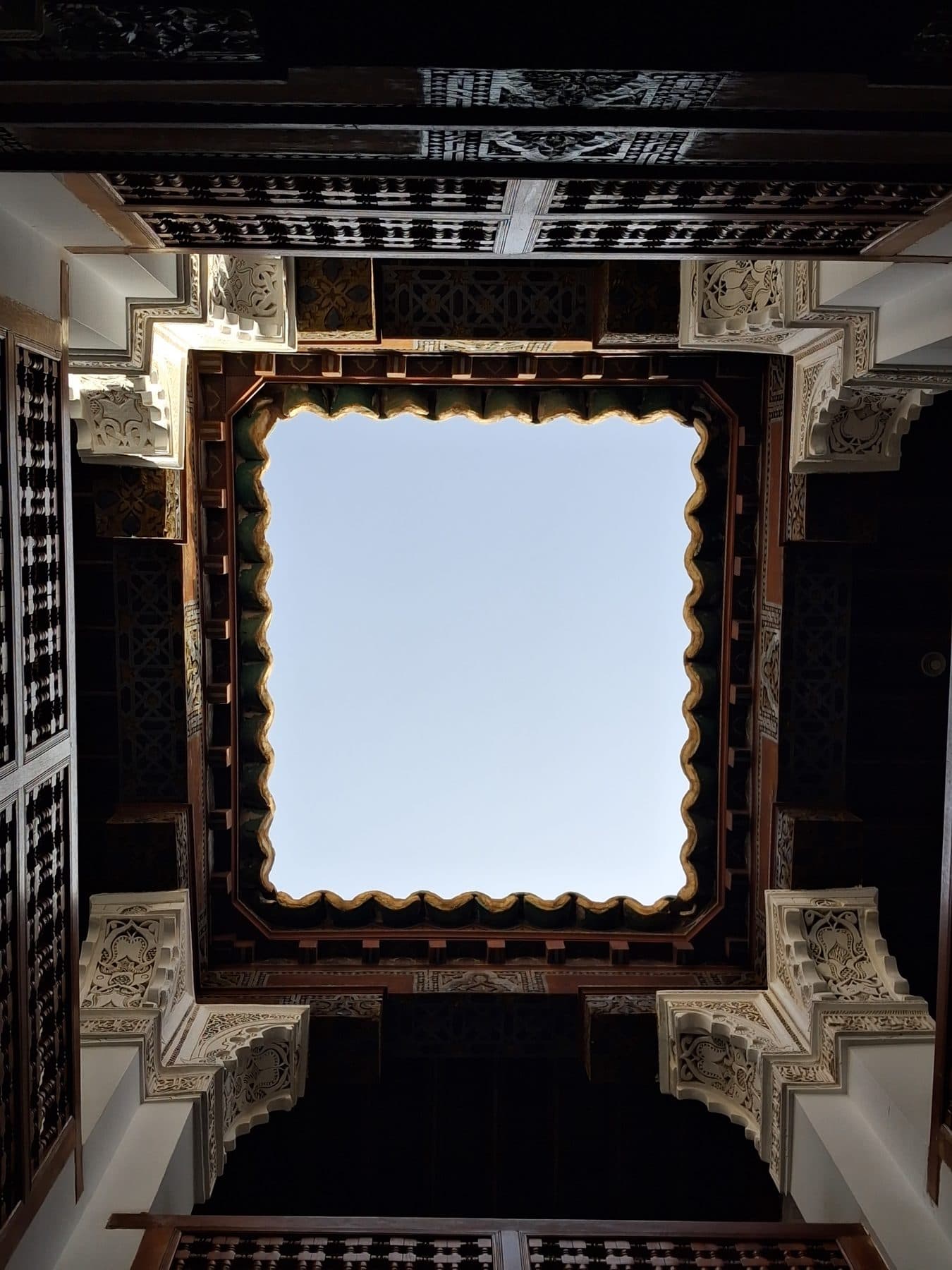 Plafond de cèdre sculpté ouvert sur le ciel, vu depuis la cour de la médersa Ben Youssef