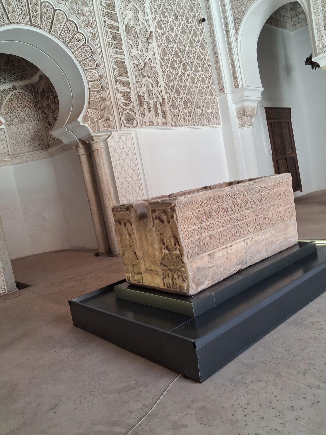 Salle de prière de la medersa Ben Youssef avec son mihrab en arc outrepassé et une vasque de pierre sculptée exposée