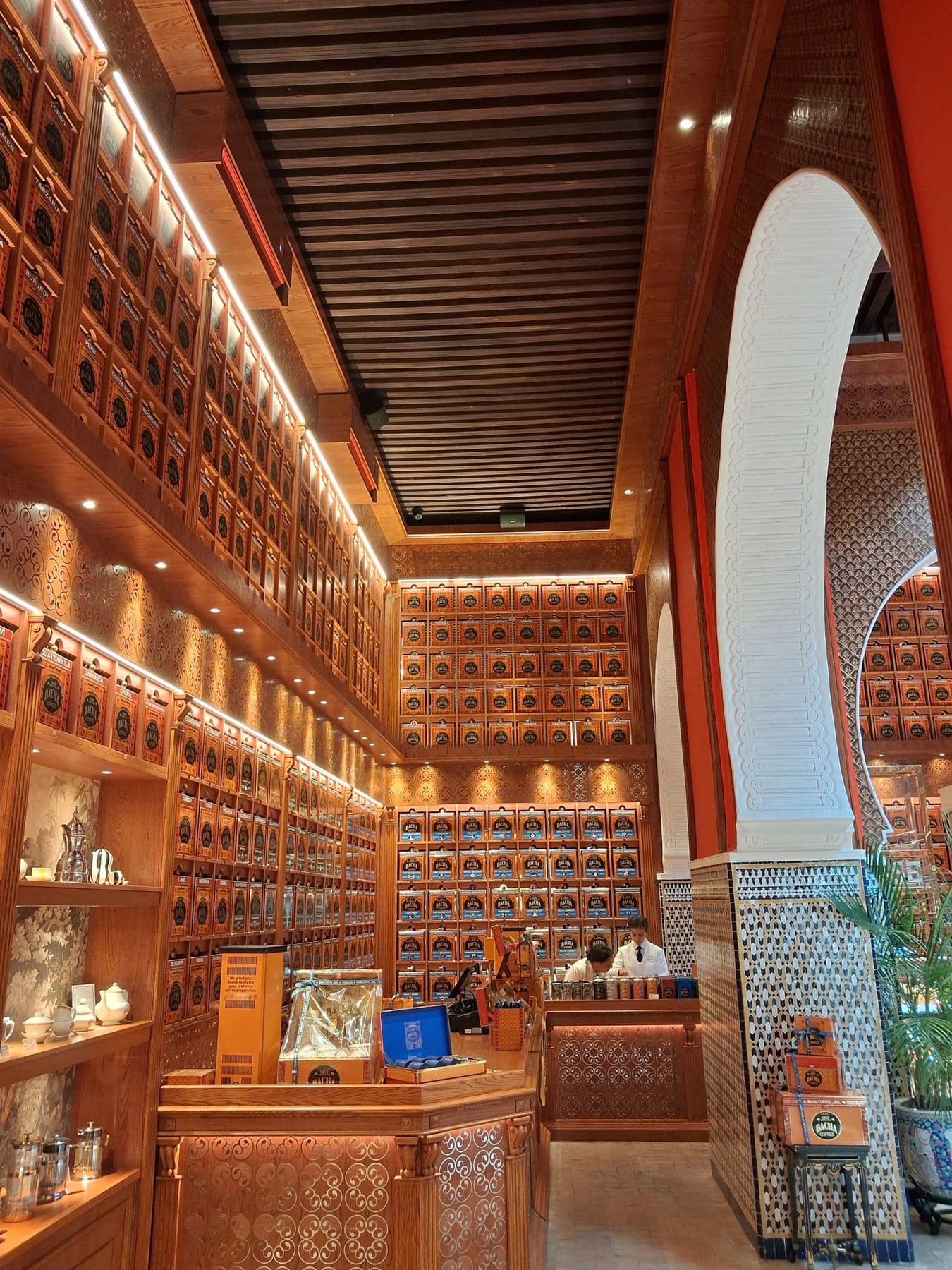 Boutique du Bacha Coffee, avec des boîtes de café alignées sur des étagères de bois, devant une arche blanche et un pilier de zellige.