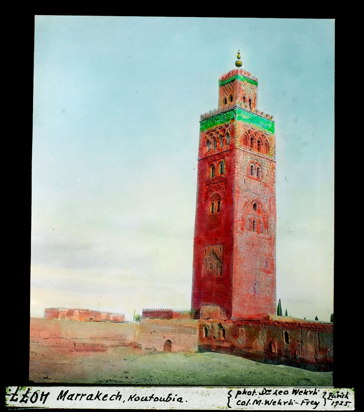 Le minaret de la Koutoubia, tour carrée aux façades rouges surmontée d'un lanternon vert, au-dessus d'un mur bas.