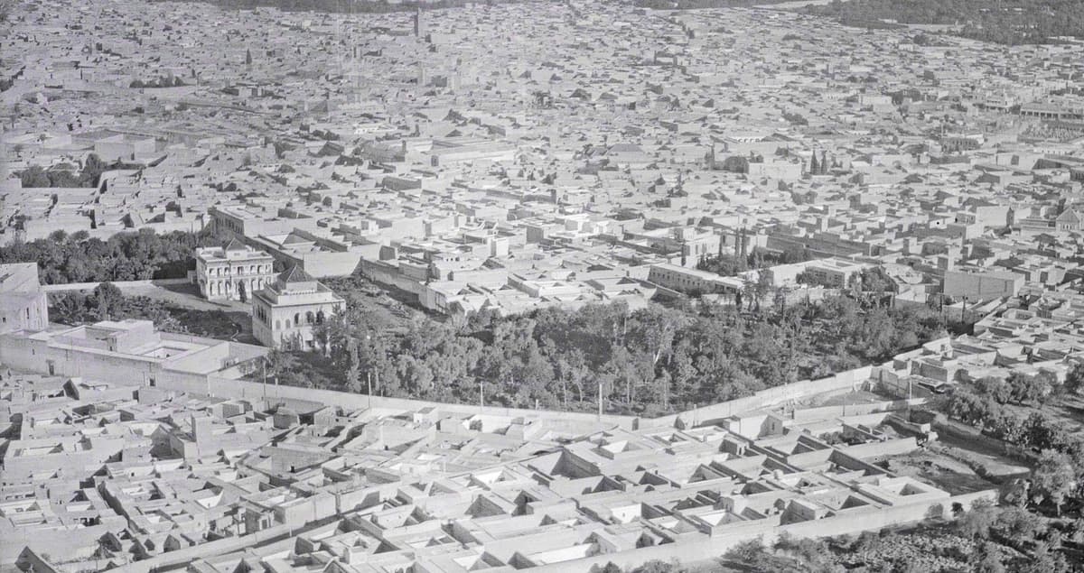 Vue aérienne en noir et blanc de toits-terrasses, avec un bâtiment à toit pyramidal près d'un jardin planté d'arbres.