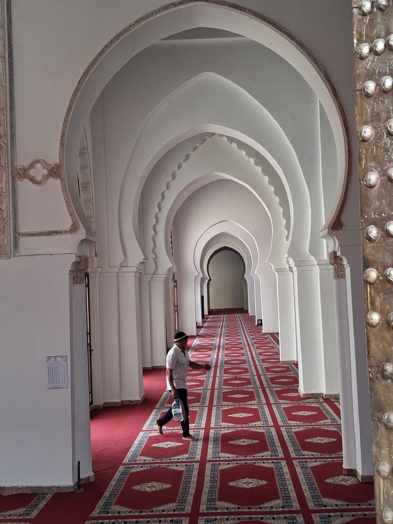 Galerie aux arcs en fer à cheval de la mosquée de la Kasbah, avec un sol couvert de tapis rouges.
