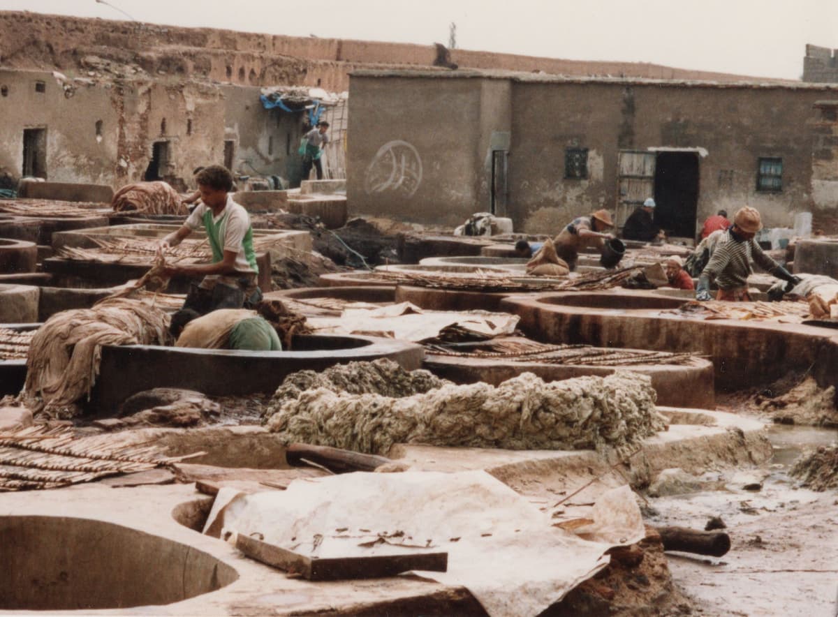 Ouvriers au travail parmi les cuves rondes des tanneries, devant des bâtiments de terre.
