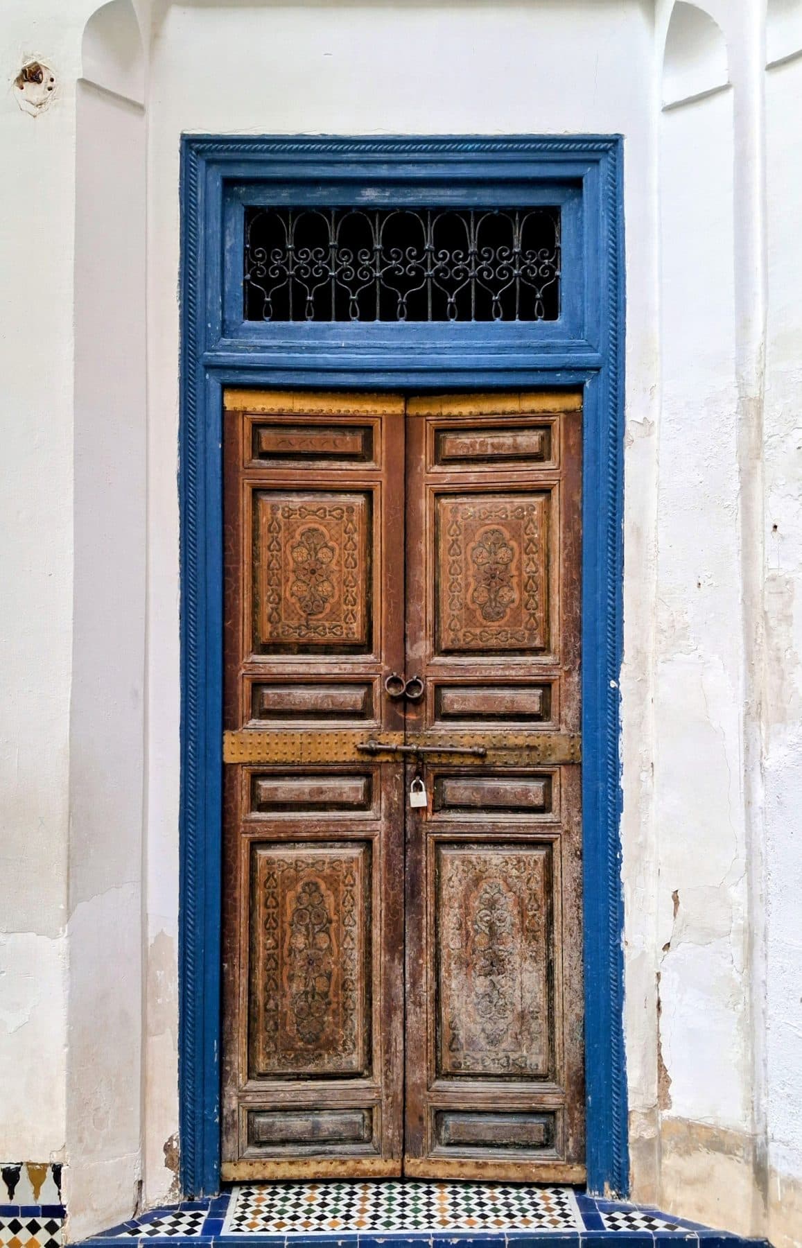 Porte en bois sculpté encadrée de bleu et surmontée d'une grille en fer forgé, au palais de la Bahia