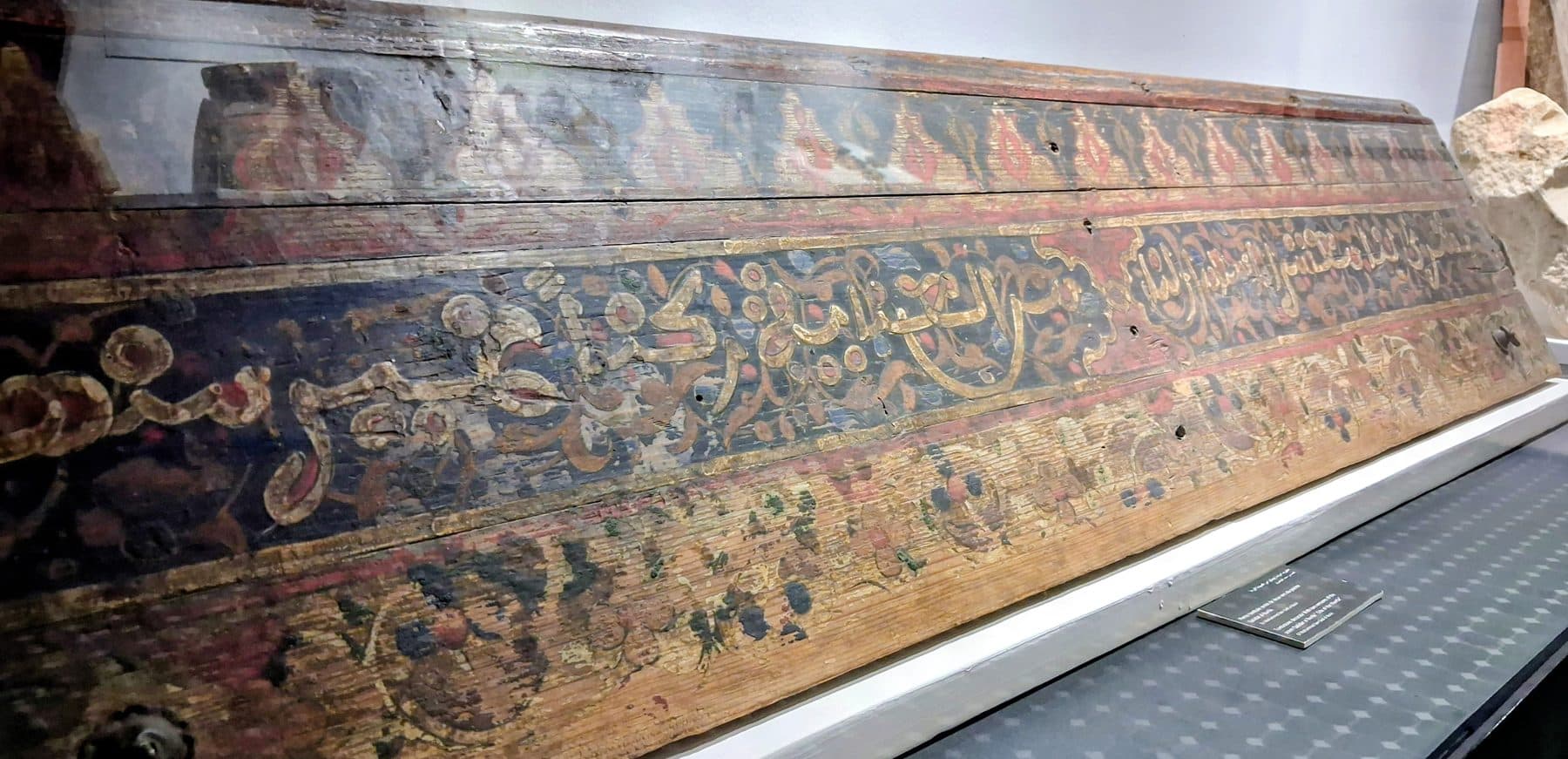 Poutre de bois peinte ornée de calligraphie dorée, conservée en vitrine au palais El Badi