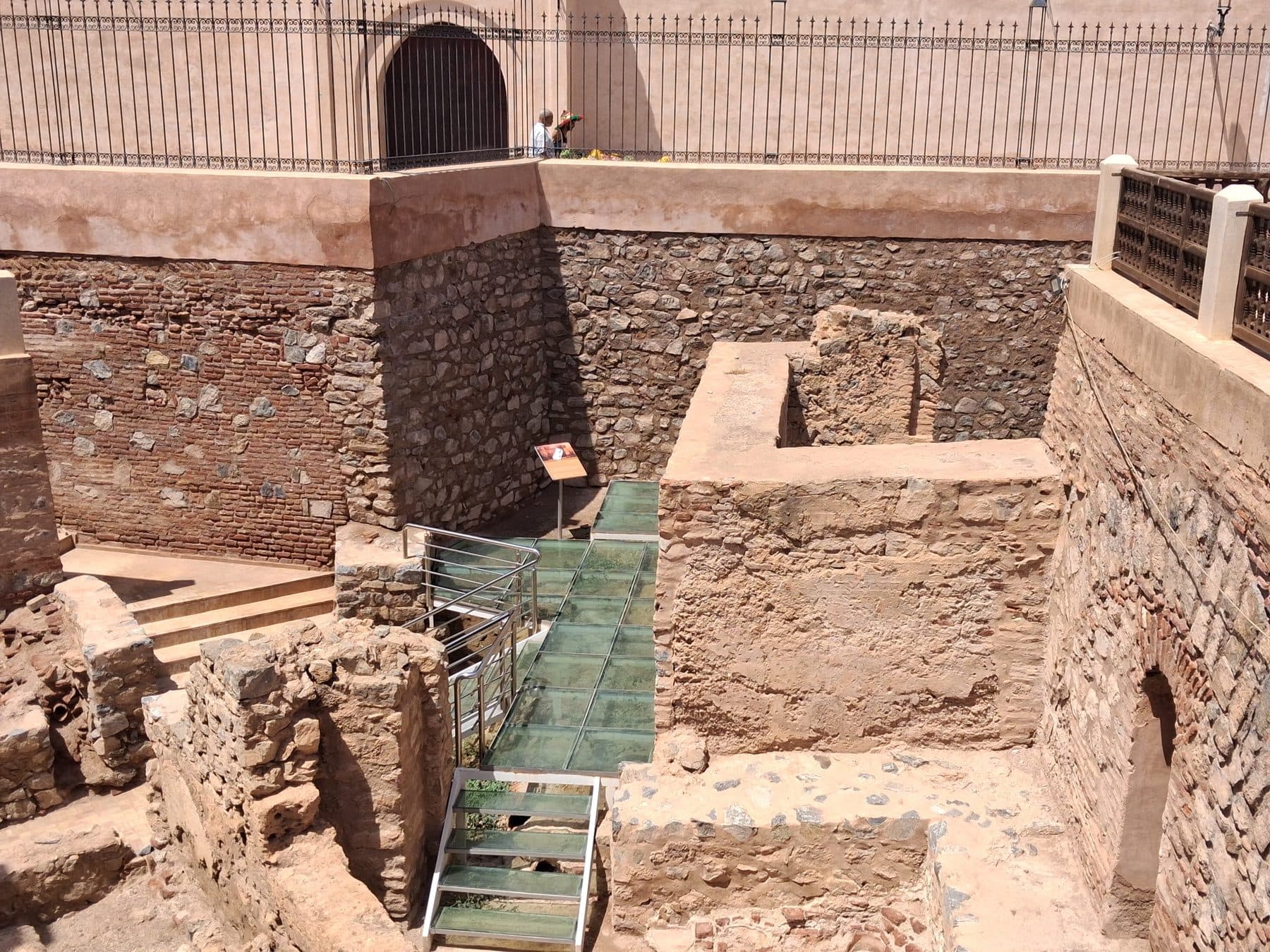 Murs de pierre et de brique mis au jour par les fouilles autour de la qoubba almoravide, avec une passerelle en verre
