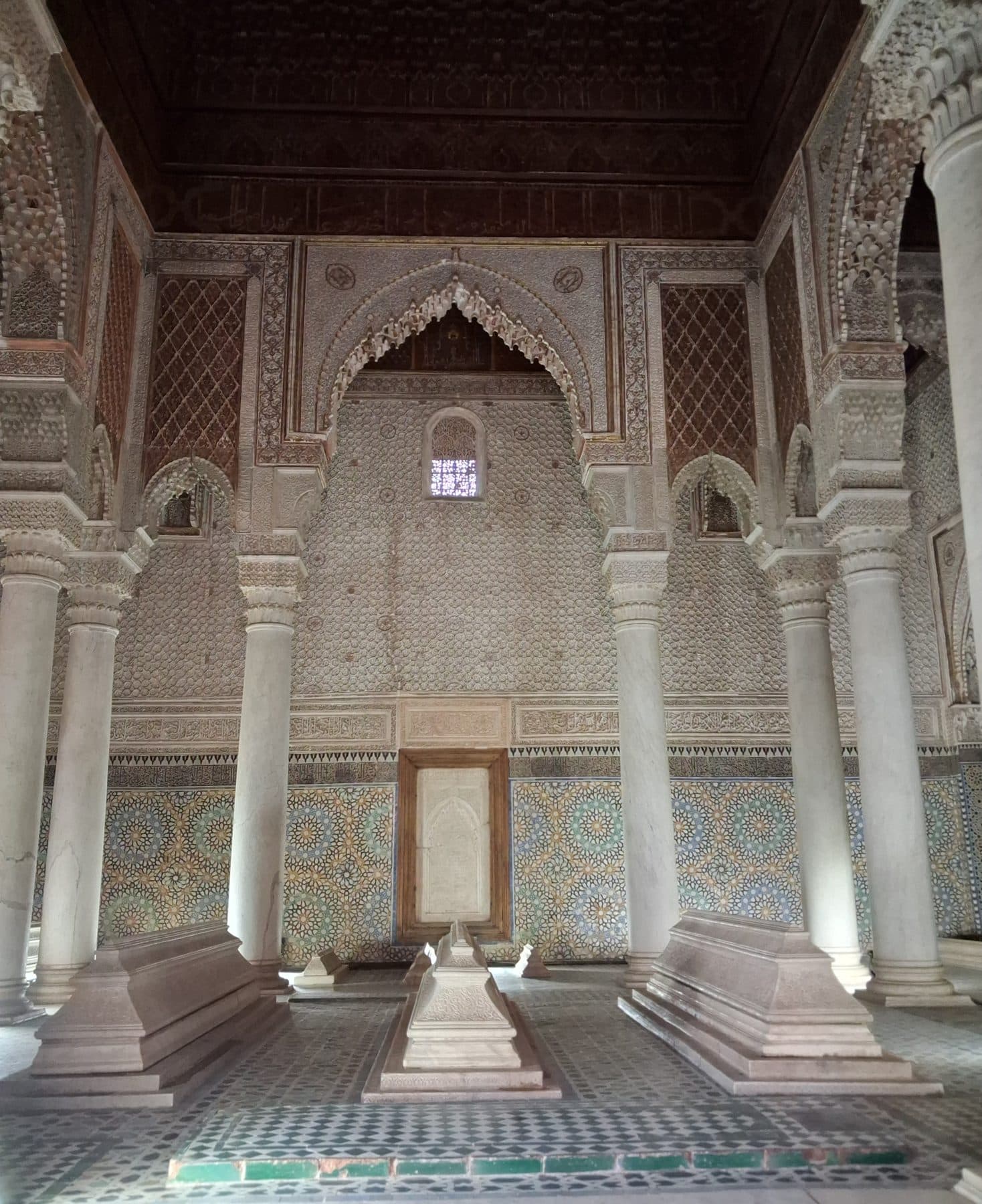 Salle des douze colonnes des tombeaux saadiens : colonnes de marbre, tombes au sol, murs de stuc sculpté et de zellige, plafond de bois