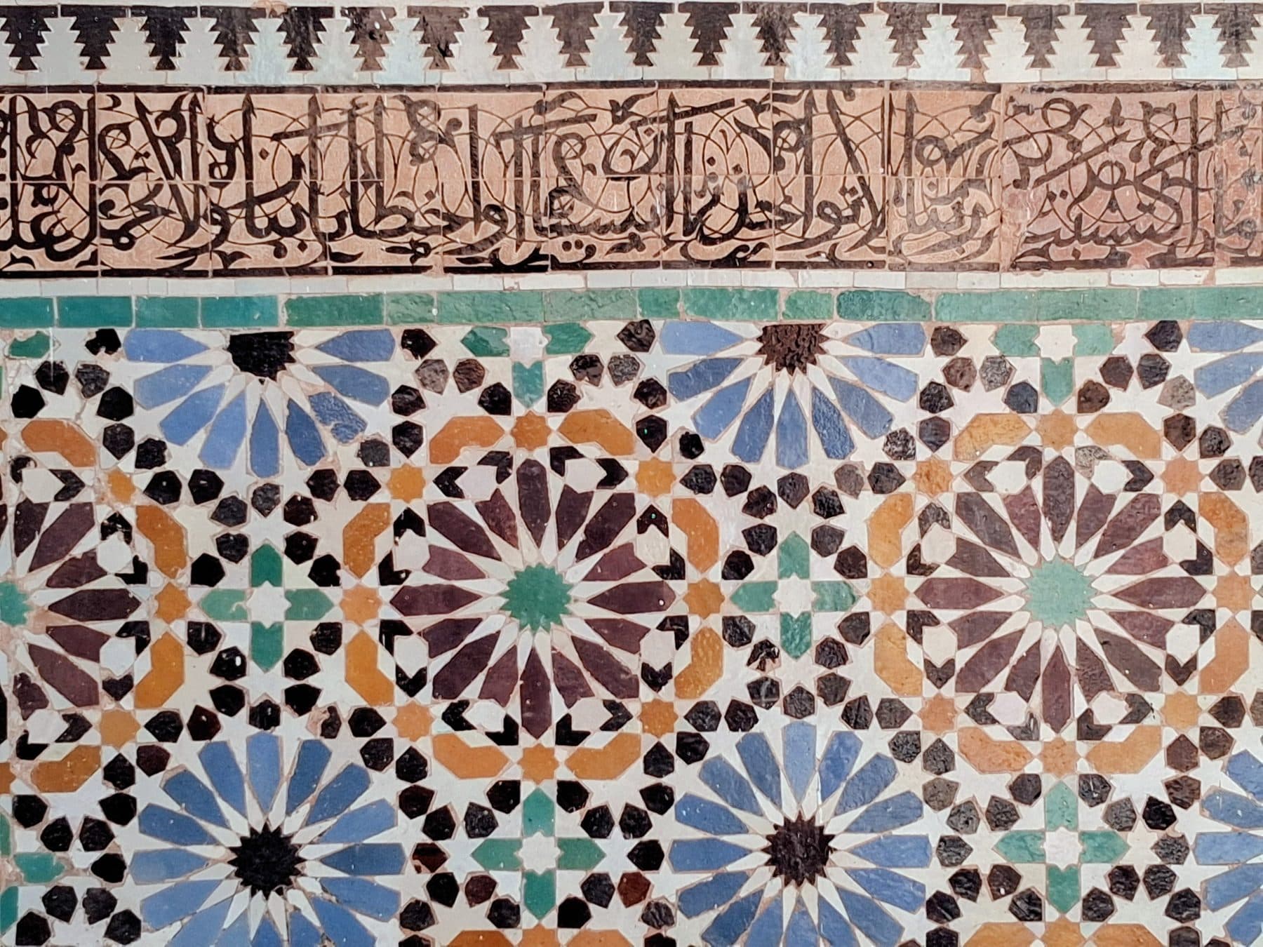 Frise de calligraphie en carreaux au-dessus d'un panneau de zellige aux étoiles bleues, brunes et vertes