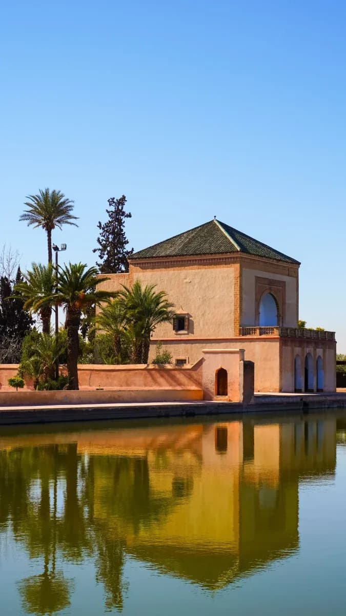 Le pavillon de la Ménara et son toit de tuiles vertes, entouré de palmiers et reflété dans le grand bassin