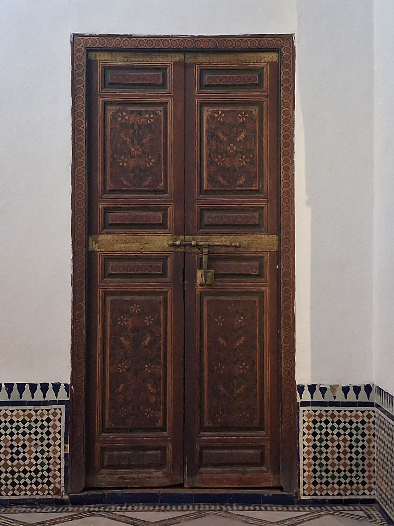 Porte à deux battants en bois peint de motifs floraux, encadrée de zellige, au palais de la Bahia